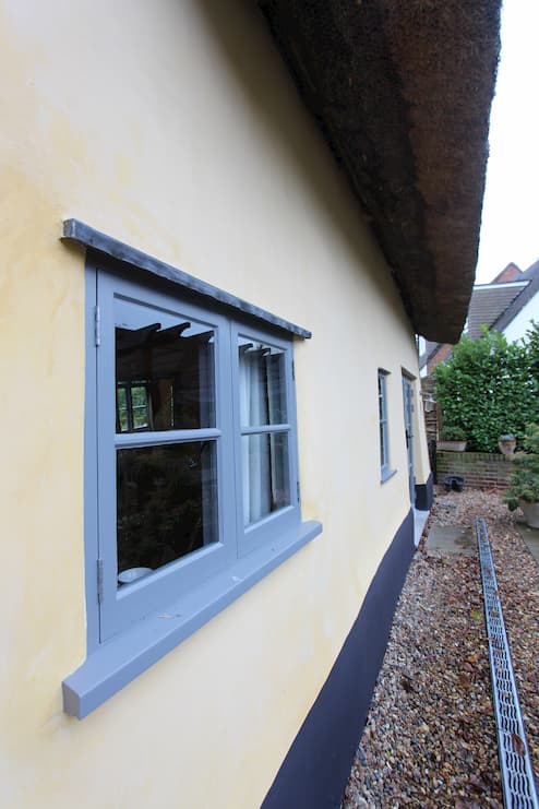 Lime render on the exterior of a thatched cottage with light blue windows